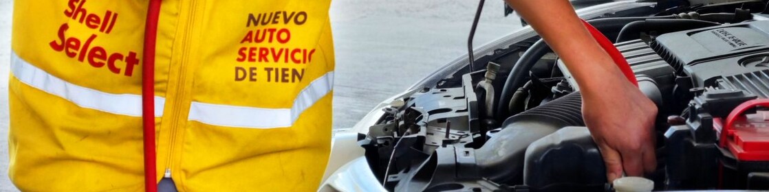 Empleado de la estación Shell, en uniforme amarillo, hace mantenimiento en el automóvil