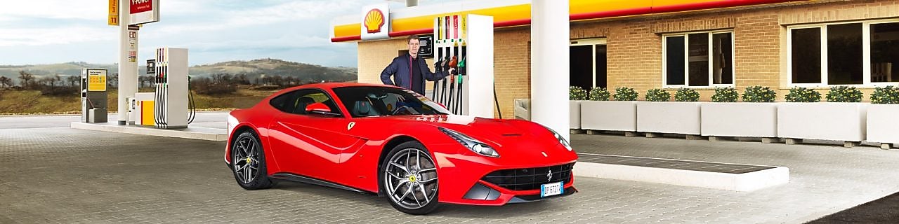 Hombre blanco com su coche Ferrari rojo en una estación de servicio de Shell