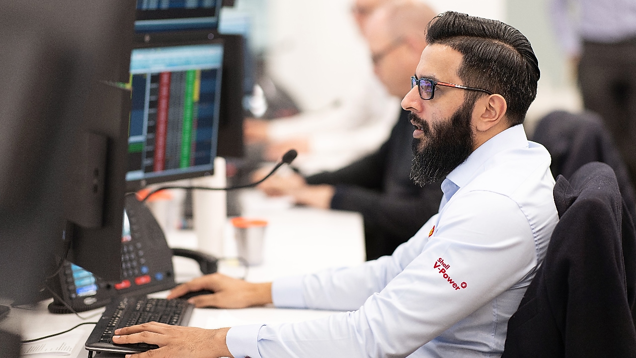 Soporte técnico de Shell GO+ Honduras atendiendo a clientes desde oficina con pantallas de datos y computadora.