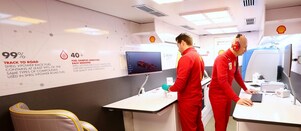 Dos hombres de uniforme rojo de la Alianza Shell y Ferrari trabajan en sus computadoras