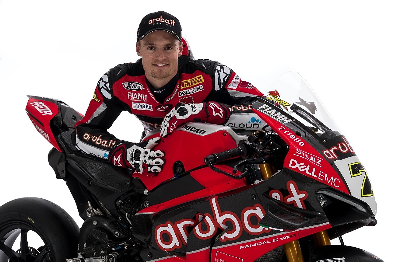 Chaz Davies, hombre blanco con pelo rubio, veste su uniforme de Ducati, una gorra y posa con su moto