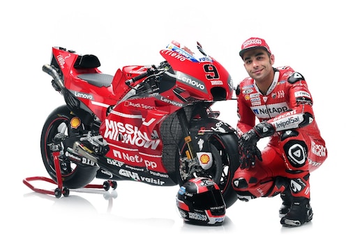 Danilo Petrucci, hombre blanco, en su uniforme de Ducati, veste una gorra y posa con su moto