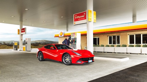 Hombre blanco com su coche Ferrari rojo en una estación de servicio de Shell