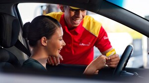 Una mujer de cabello negro en su auto es recibida por un empleado de Shell