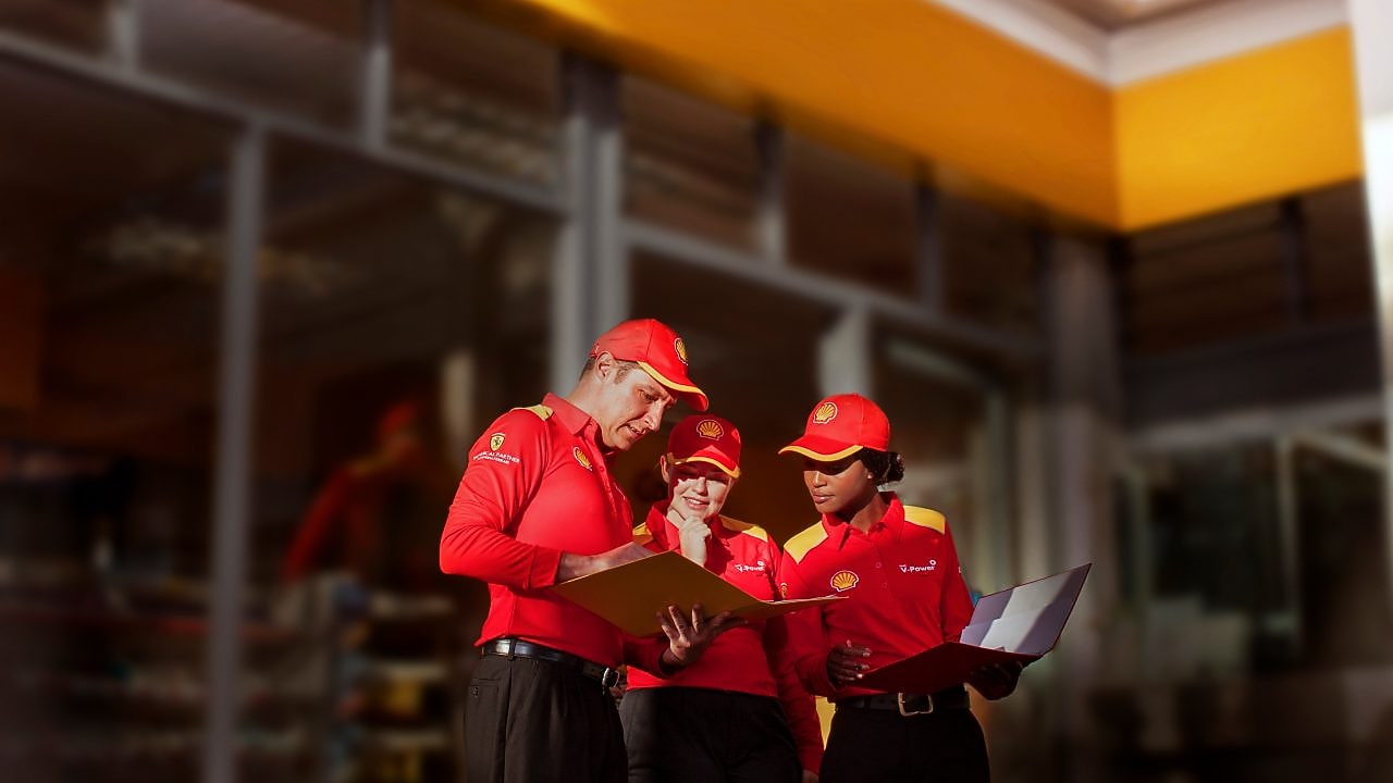 Tres empleados de Shell con uniforme rojo trabajando en una estación de servicio