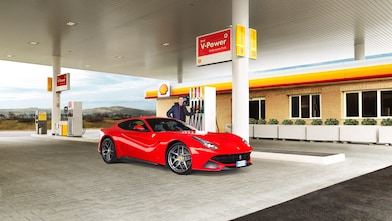 Hombre blanco com su coche Ferrari rojo en una estación de servicio de Shell